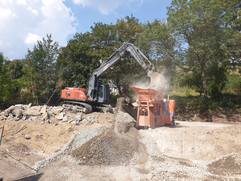 Roter ATLAS-Bagger beschickt die orange Backenbrecheranlage von WEGENER