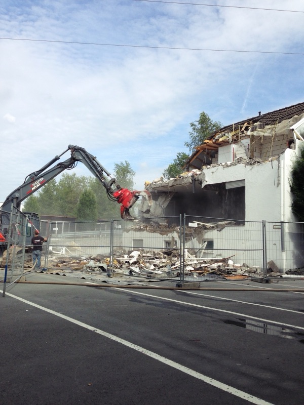 Abbruchbagger trägt das Obergeschoss hinter dem Bauzaun ab
