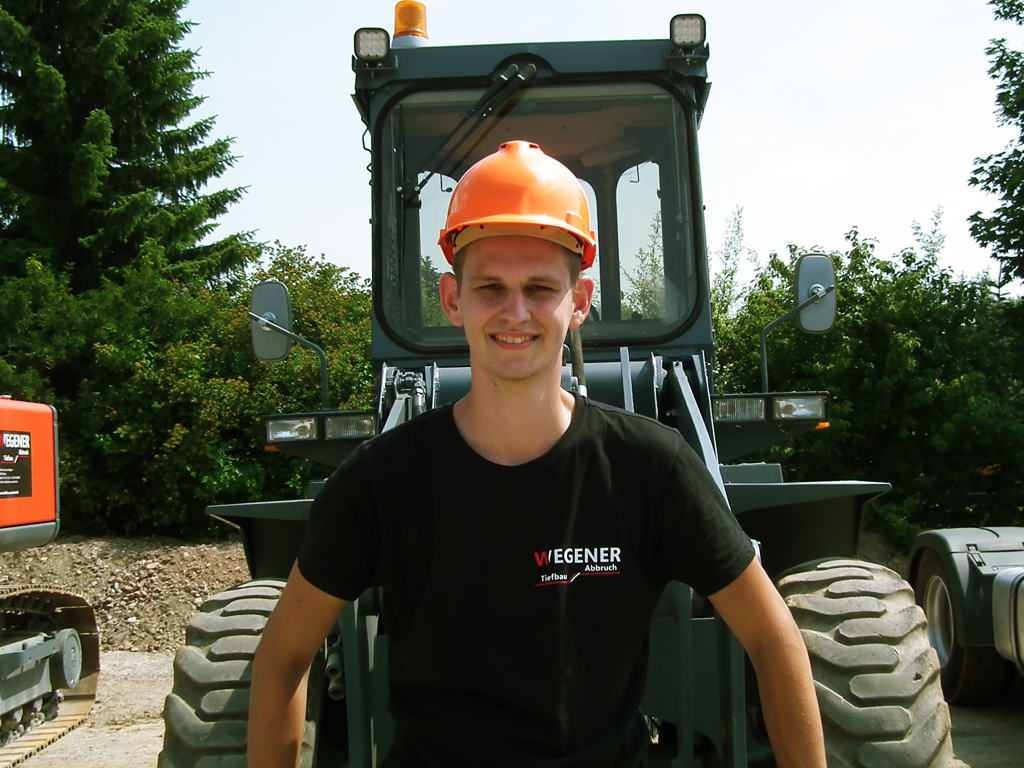 Steve Wegener, Juniorchef, mit Helm und WEGENER-Shirt vor einem Bagger